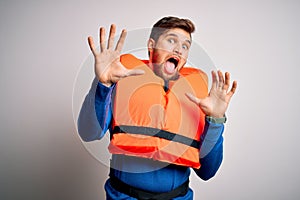 Young blond tourist man with beard and blue eyes wearing lifejacket over white background afraid and terrified with fear