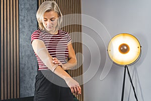 young blond woman adjusting her elbow support brace at home, self-treatment concept