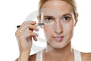 Young blond woman applying concealer under her eyes