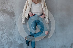 Young blond woman in a beige fashionable leather jacket in a white trendy t-shirt in blue ripped jeans