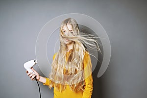 Young blond woman blow-drying her hair