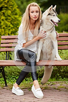 Young blond woman with dog Husky sits on bench in