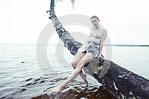Young blond woman hanging on birch tree at lake shore, summer vacations outdoor lifestyle