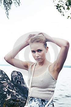 Young blond woman hanging on birch tree at lake shore, summer vacations outdoor lifestyle