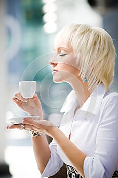 Young blond woman holding cup and tasting coffee