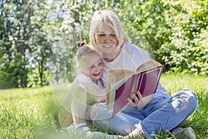 Young blond woman with little daughter lie on the grass with a book in the park. Love and tenderness. Camping on a sunny summer