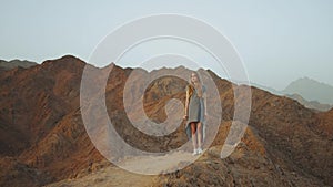 Young blond woman in long dress walks on top of mountain. Mountain landscape with sunset, slow motion, full hd