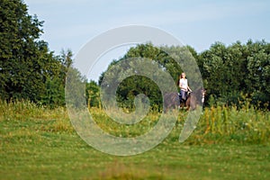 Young blond woman with long hair jockey rider jumping on a bay horse