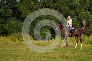 Young blond woman with long hair jockey rider jumping on a bay horse