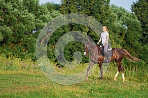 Young blond woman with long hair jockey rider jumping on a bay horse