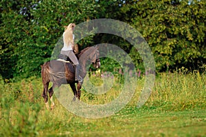 Young blond woman with long hair jockey rider jumping on a bay horse