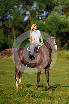 Young blond woman with long hair jockey rider jumping on a bay horse