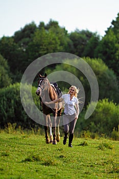 Young blond woman with long hair jockey rider jumping on a bay horse