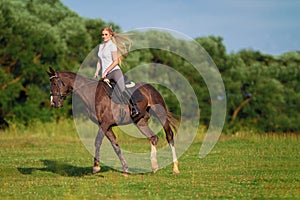 Young blond woman with long hair jockey rider jumping on a bay horse