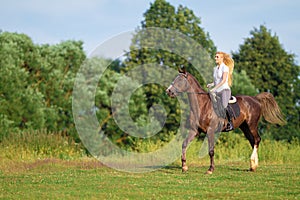 Young blond woman with long hair jockey rider jumping on a bay horse