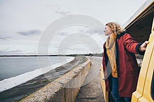 Young blond woman looking out of camper van overlooking the sea