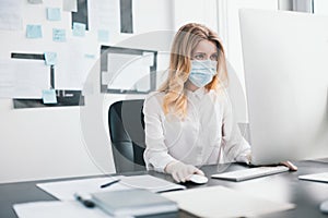 Young blond woman manager in medical protection mask and gloves works in office during Covid-19 epidemy, virology concept