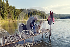 Young blond woman on a motorcycle on a pier on a lake in the mountain with two dogs