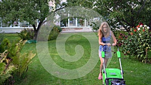 Young blond woman mowing lawn in residential back garden on summer evening