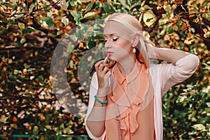 Young blond woman paints lips while standing on the street