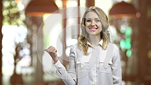 Young blond woman in restaurant pointing back with her thumb.