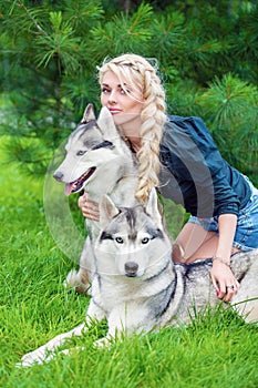 Young blond woman sits embracing two husky dogs on