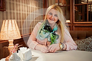 Young blond woman sits at table in cosy photo