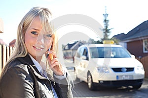 Young blond woman with smartphone and taxicab