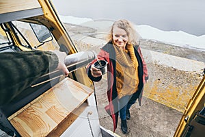 Young blond woman standing next to camper van overlooking the sea