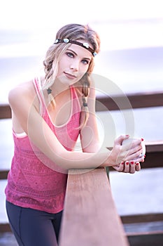 A young blond woman standing on a pier with a cup of coffee and her workout outfit.