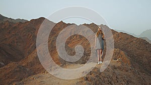 Young blond woman standing on top of mountain. Mountain landscape with sunset, slow motion, 4k