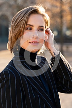 Young blond woman in striped jacket and sweater straightens her hair in park
