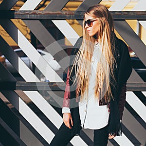 Young blond woman in sunglasses and a fashionable outfit posing on the street warm spring evening. Fashion blogger.