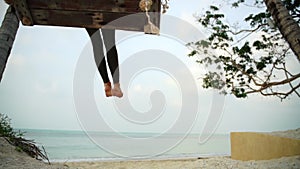 Young blond woman swinging on big swings at the beach with a sea view.