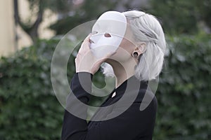 Young blond woman taking off a mask. Pretending to be someone else concept. outdoors.