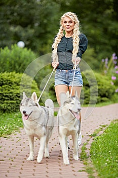 Young blond woman with two Husky dogs on dog-leads