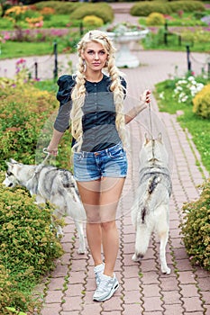 Young blond woman with two Husky dogs on dog-leads