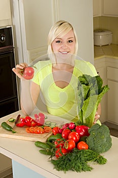 Young blond woman with vegetables on kitchen