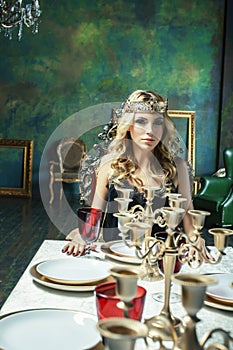 Young blond woman wearing crown in fairy luxury interior with em