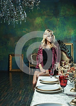 Young blond woman wearing crown in fairy luxury interior with em