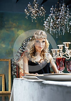 Young blond woman wearing crown in fairy luxury interior with em