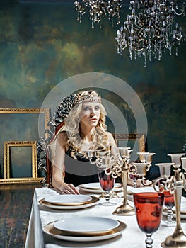 Young blond woman wearing crown in fairy luxury interior with empty antique frames total wealth