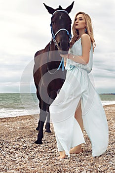 Young blond woman wears elegant dress, posing with black horse