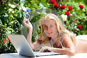 Young blond woman in white bikini lying on sunbed with laptop