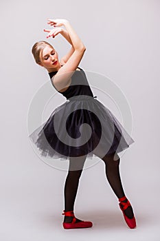 Young blonde ballerina girl dance and posing in black tutu and ballet shoes on grey background