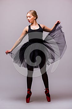 Young blonde ballerina girl dance and posing in black tutu and ballet shoes on grey background.