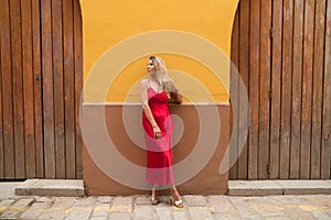 Young, blonde, beautiful woman in a red dress is visiting seville. The woman is posing for the camera very elegant for the photos