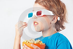 Young blonde boy in 3D glasses eating popcorn