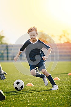 Young blonde boy kicking soccer ball on drill. Kids playing football training game on the school sports pitch