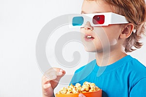 Young blonde boy in stereo glasses eating popcorn